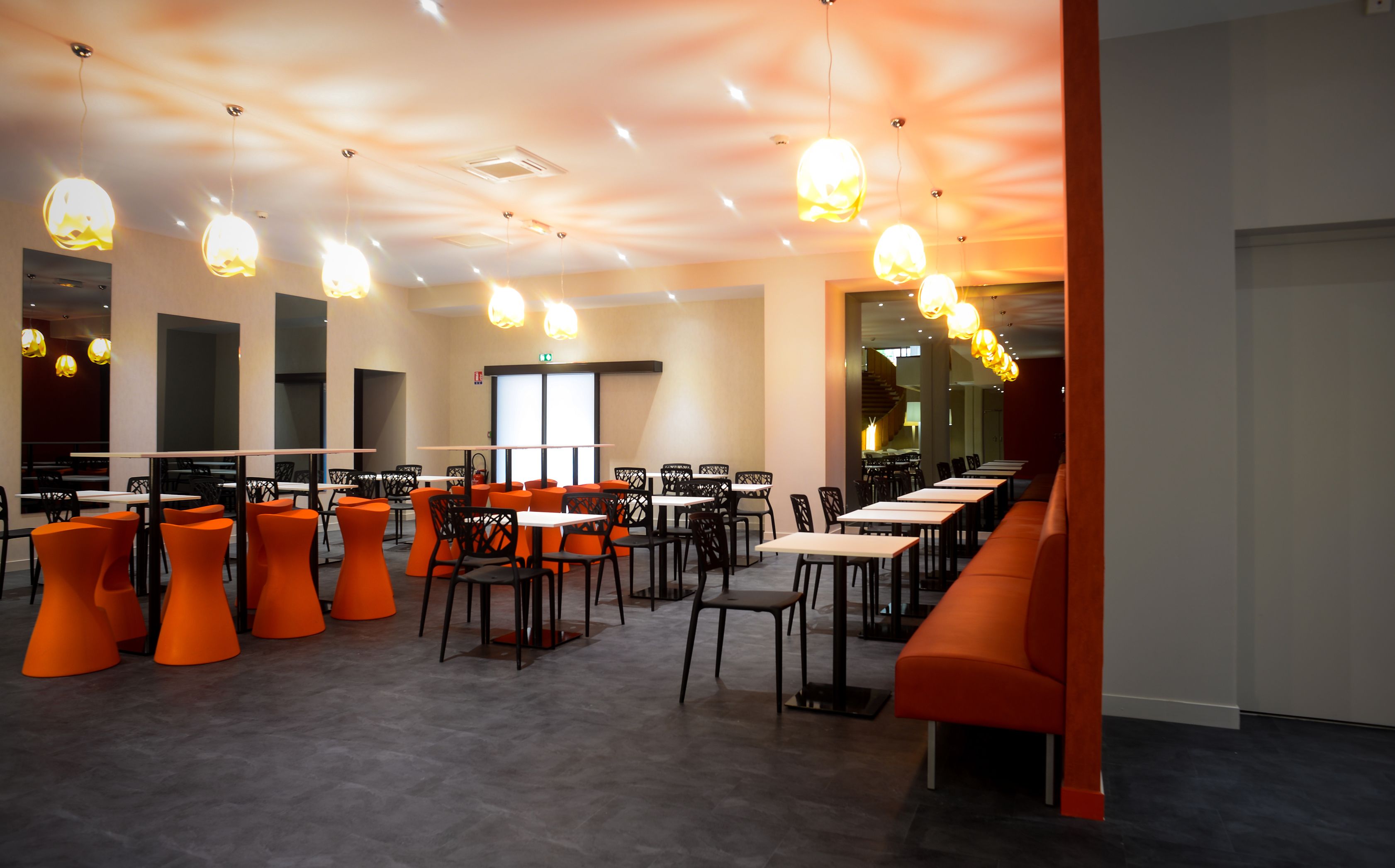 Un restaurante moderno con sillas y mesas anaranjadas, iluminación colgante y vistas a la ciudad.