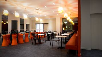 Un restaurante moderno con sillas y mesas anaranjadas, iluminación colgante y vistas a la ciudad.