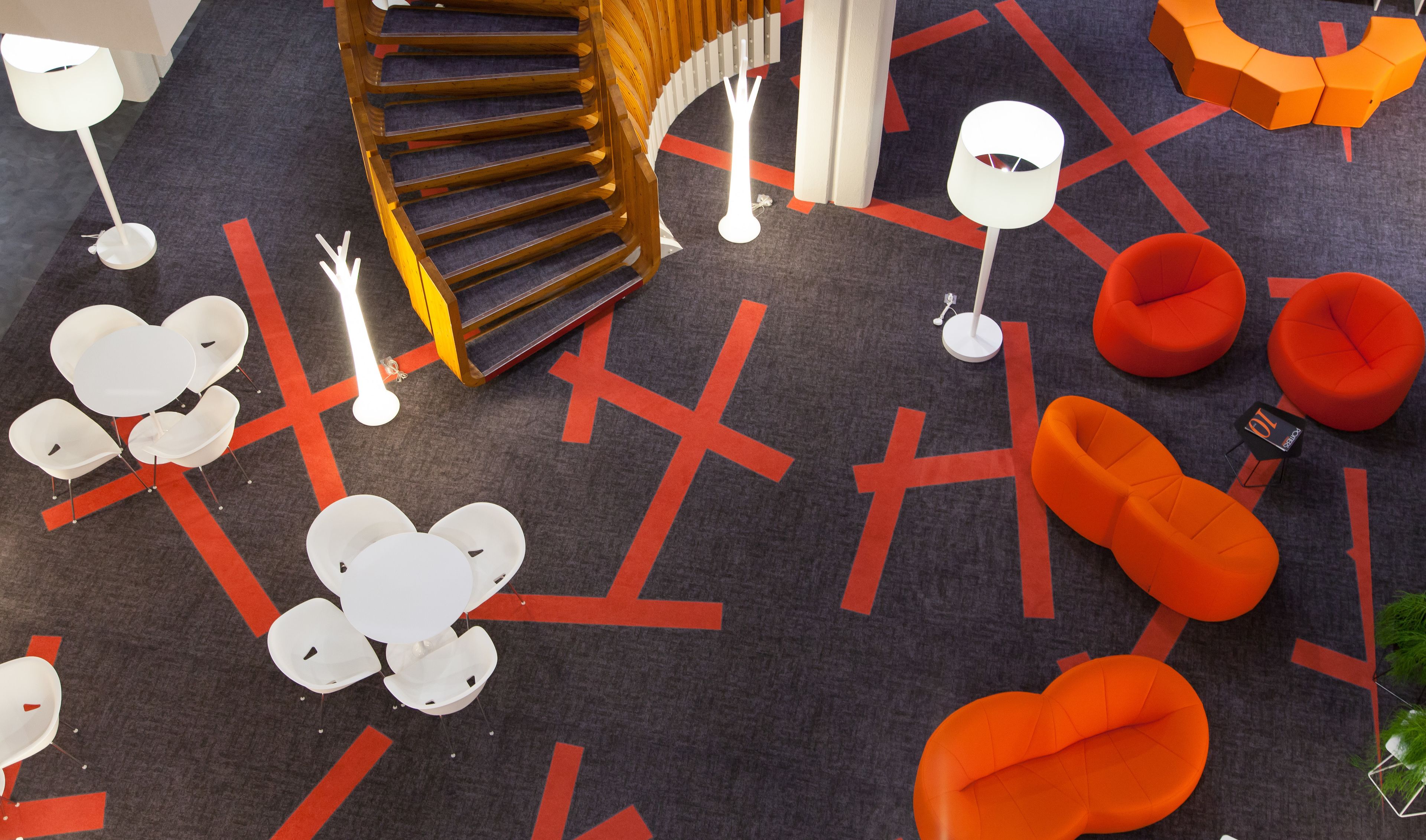 Un intérieur moderne avec un escalier en colimaçon, des sièges blancs et orange, et un tapis à motifs géométriques.
