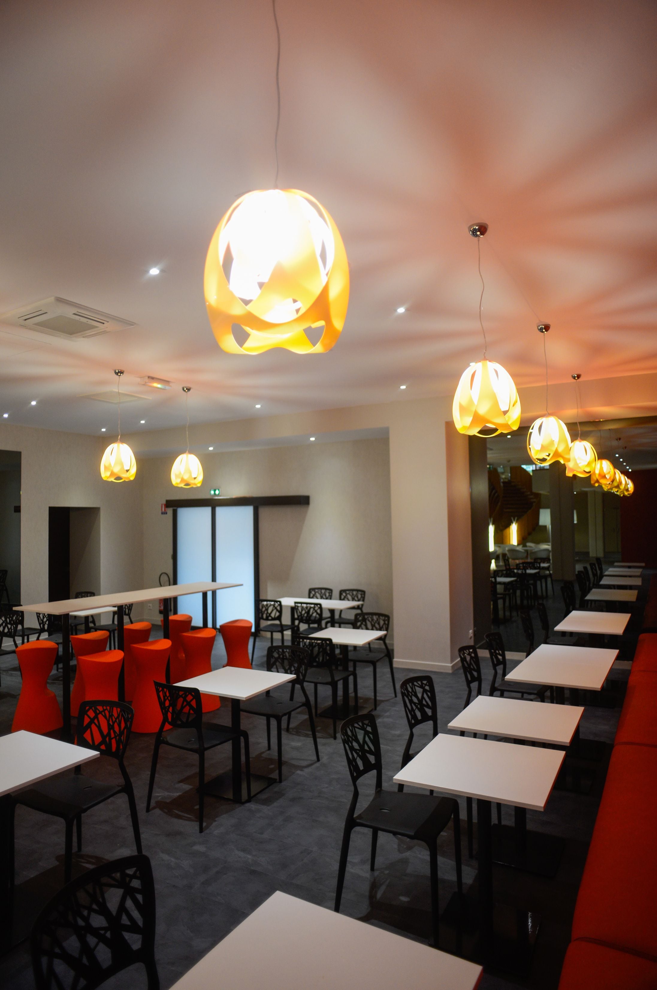 A restaurant with multiple tables and chairs, overhead lighting, and a modern interior design.