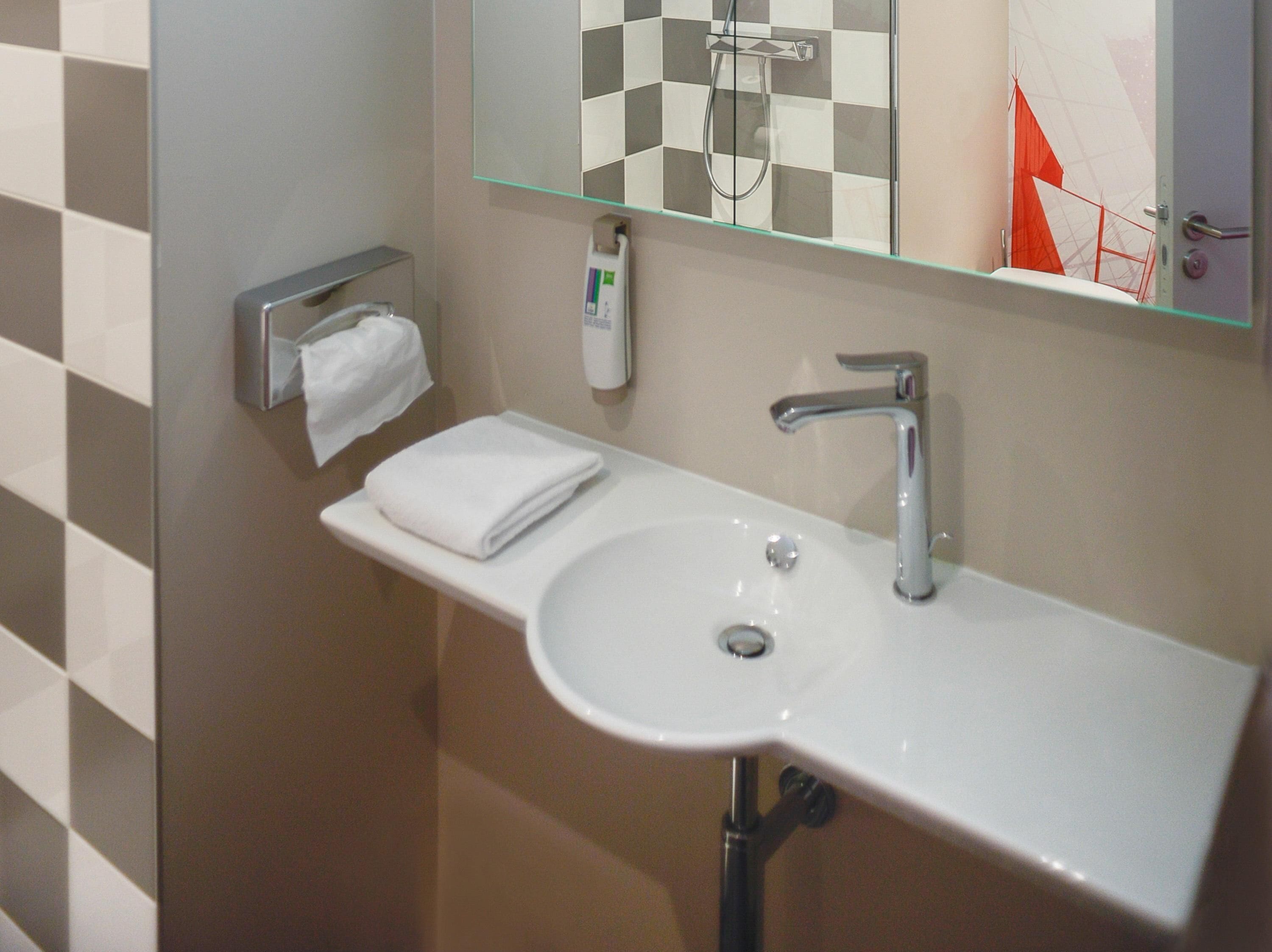 Une salle de bain avec un lavabo blanc, un miroir, un distributeur de serviettes et une pomme de douche.