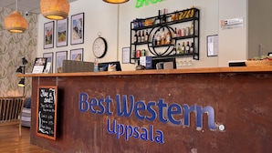 A reception area with a wooden counter, hanging wicker lamps, framed pictures on the wall, and a clock. - Best Western Uppsala (Uppsala)