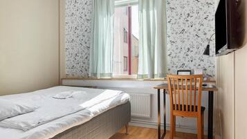 A bedroom with a single bed, a window with curtains, a desk with a chair, and a radiator.