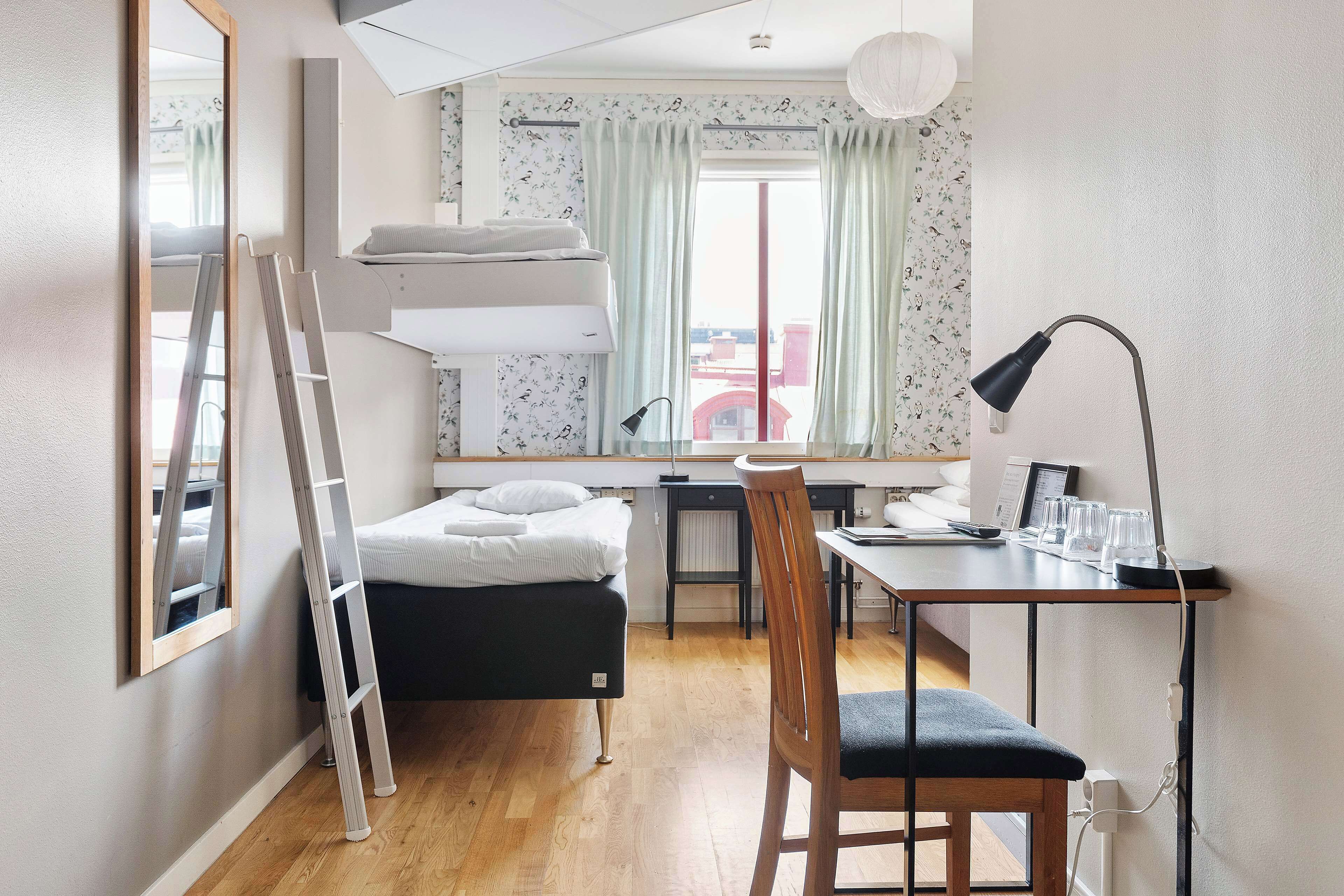 A compact bedroom with a bunk bed, a desk with a chair, and a bedside table.