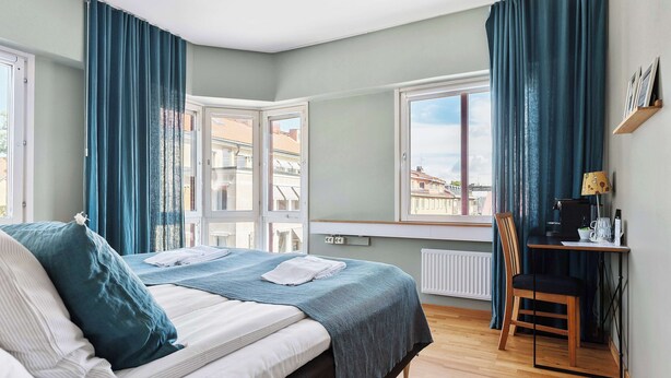 A bedroom with a bed, a desk, a chair, and a view of buildings through the window. - Best Western Uppsala (Uppsala)