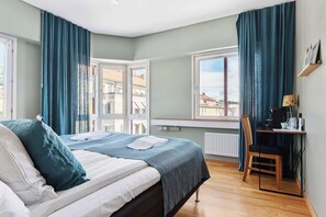 A bedroom with a bed, a desk, a chair, and a view of buildings through the window. - Best Western Uppsala (Uppsala)