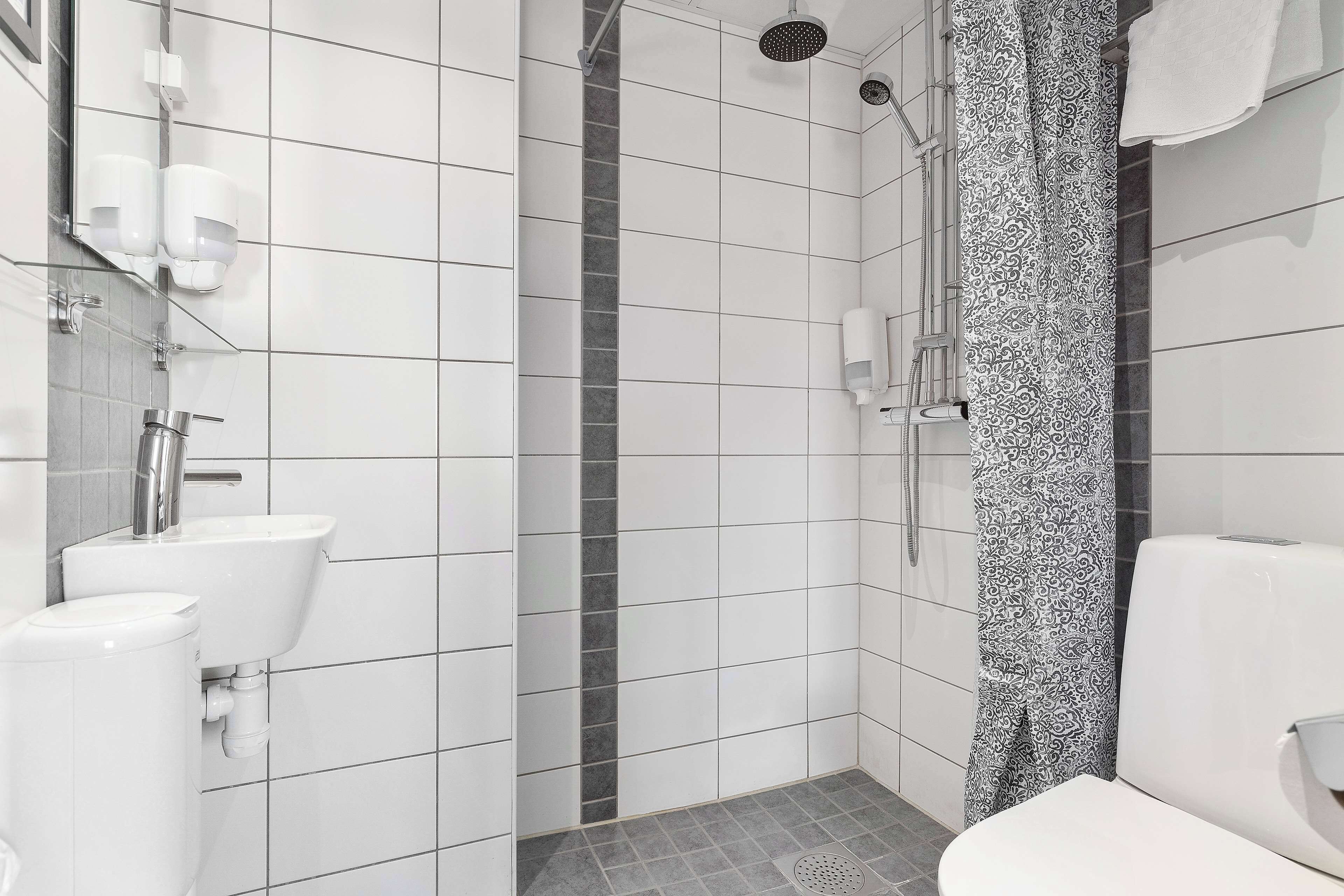 Un baño moderno con azulejos blancos, ducha, inodoro y lavamanos.