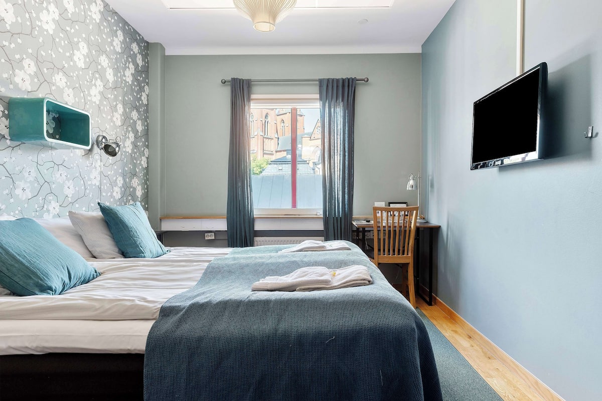 A hotel room with a bed, a desk, a TV, and a window with curtains.