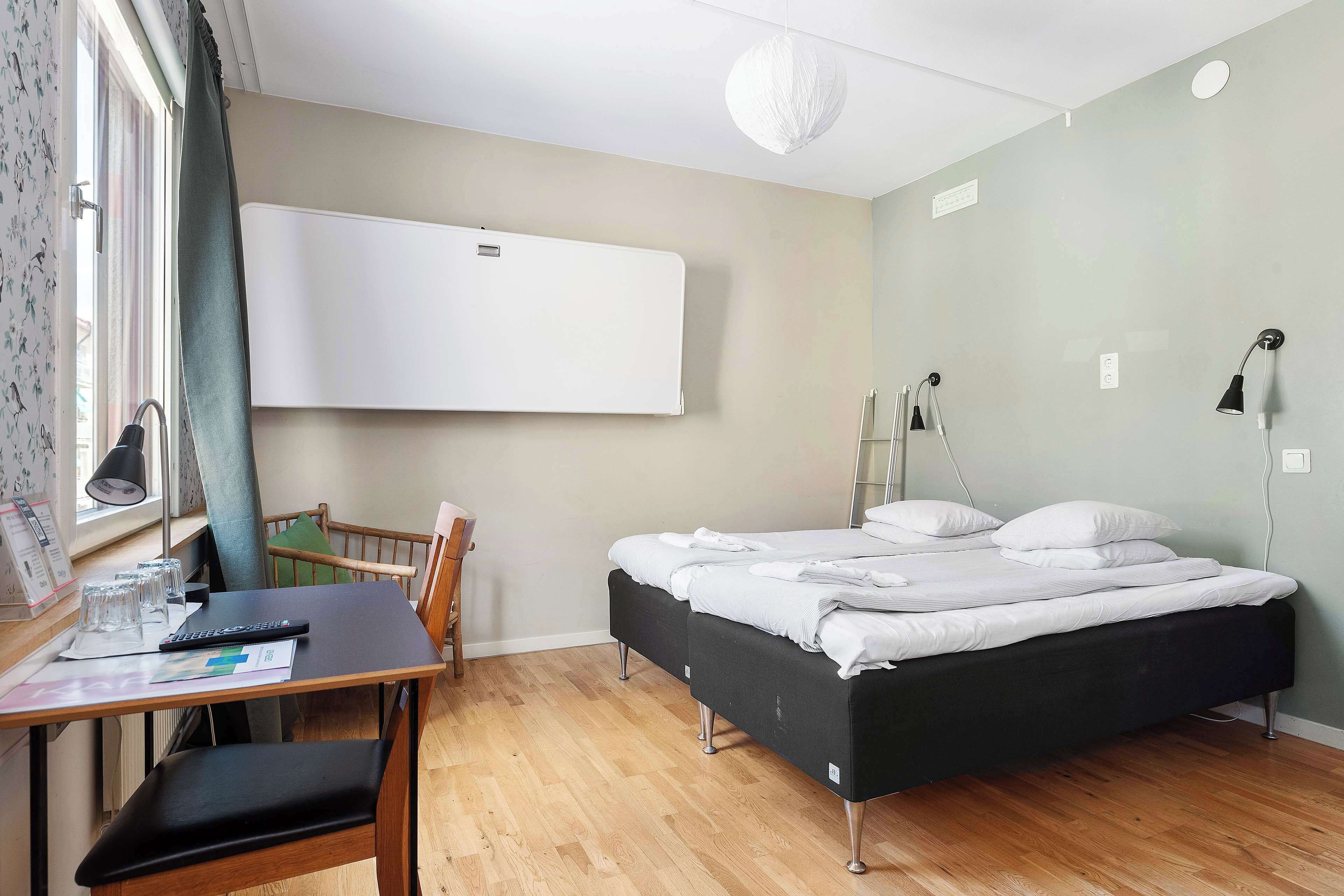 Une chambre à coucher comprenant un lit, un bureau avec une chaise, une fenêtre avec des rideaux, un climatiseur fixé au mur et une lampe de chevet.