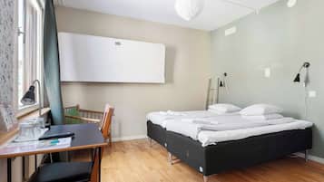 A bedroom with a bed, a desk with a chair, a window with curtains, a wall-mounted air conditioner, and a bedside lamp.