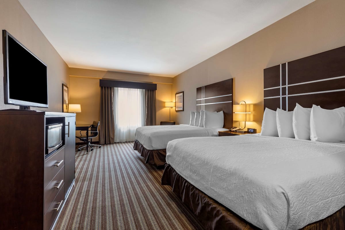 A hotel room with two beds, a TV, a desk, and a window with curtains.