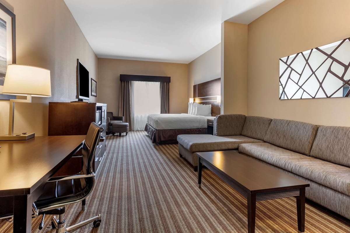 A hotel room with a bed, a sofa, a desk with a chair, a TV, and a lamp.