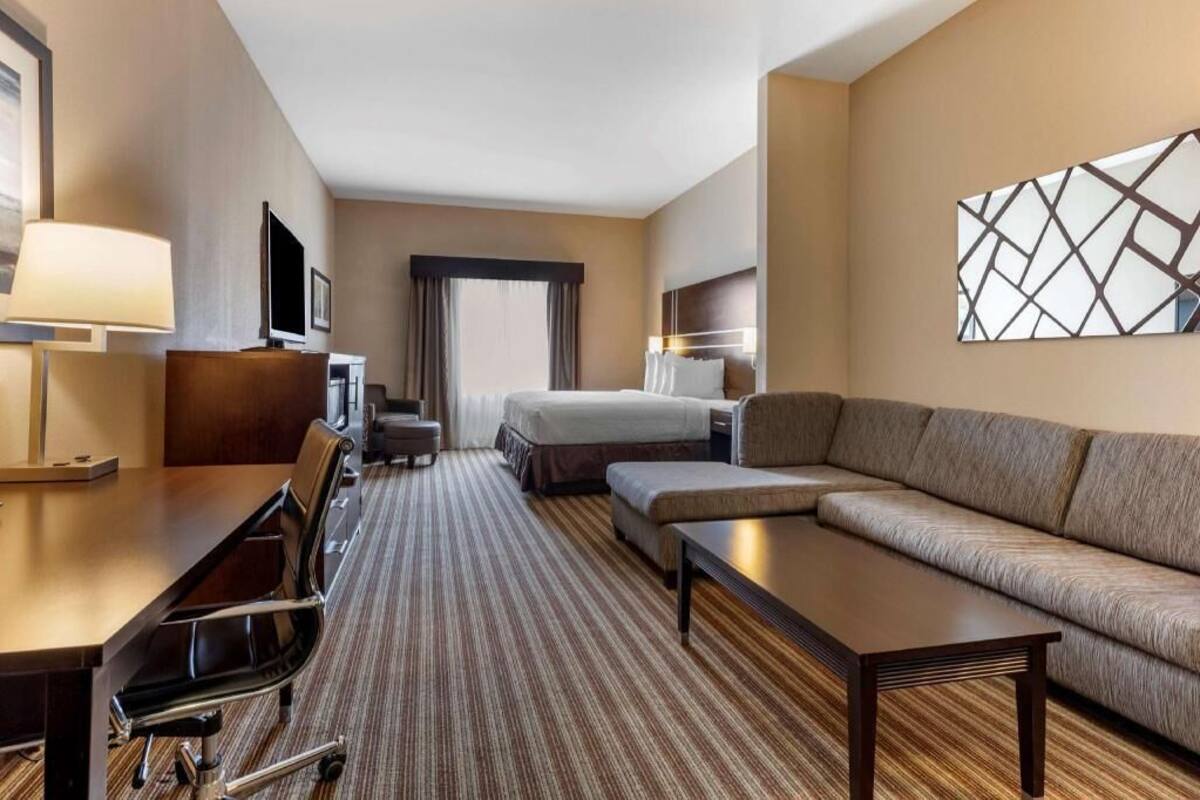 A hotel room with a bed, a sofa, a desk with a chair, a TV, and a lamp.