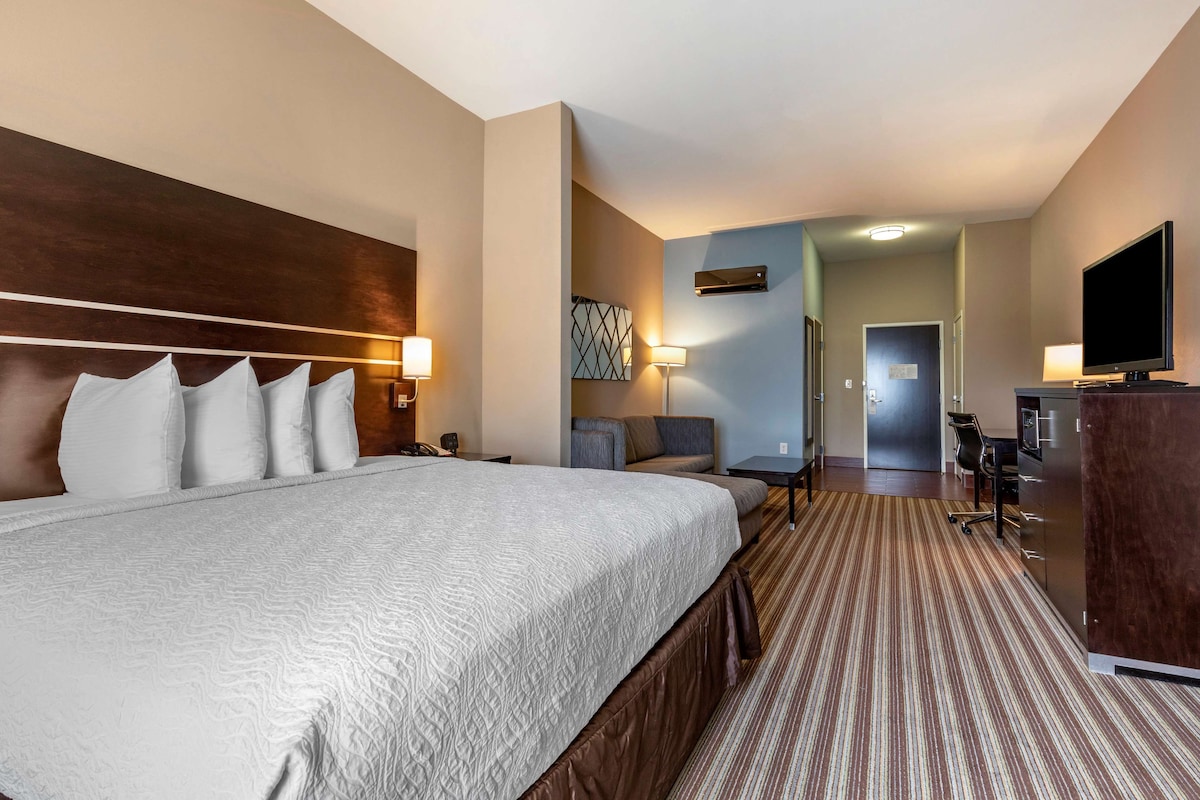 A hotel room with a large bed, a desk, a chair, a television, and a wardrobe.