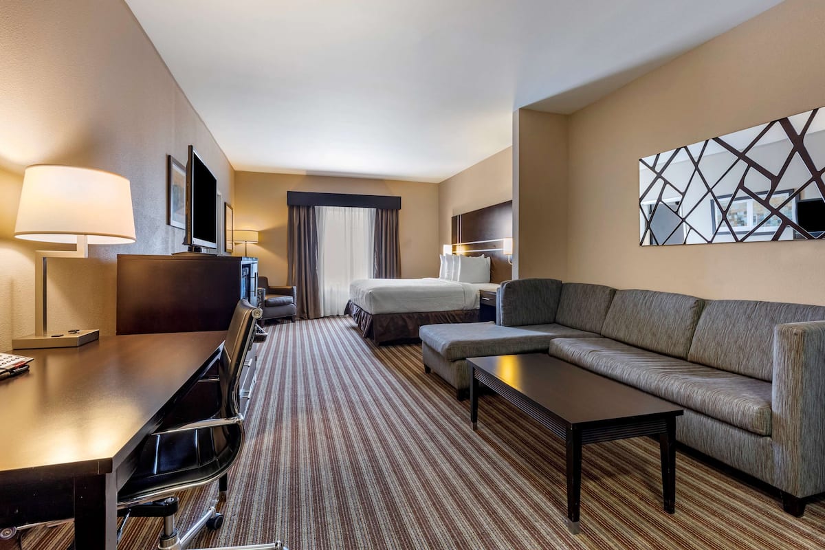 A hotel room with a bed, a sofa, a desk with a chair, a TV, and a lamp.
