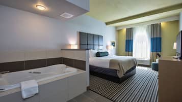 A hotel room with a large bathtub, a bed with a headboard, a desk with a computer, and a window with curtains.