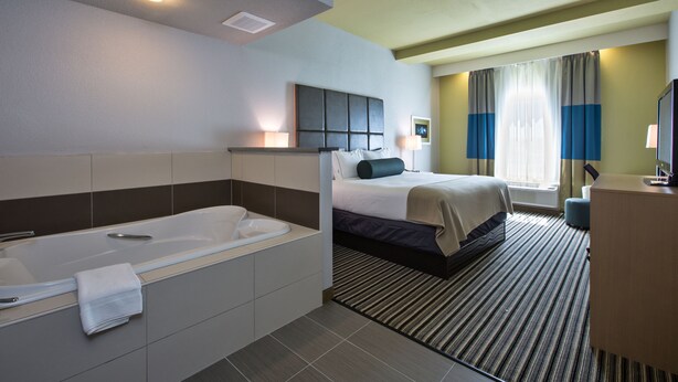 A hotel room with a large bathtub, a bed with a headboard, a bedside table, a desk, and a window with curtains. - Holiday Inn Express Hotel & Suites, Carlisle-Harrisburg Area by IHG (Carlisle)