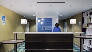 A hotel reception desk with a blue sign, two side tables, and a check-in/out sign. - Holiday Inn Express Hotel & Suites, Carlisle-Harrisburg Area by IHG (Carlisle)