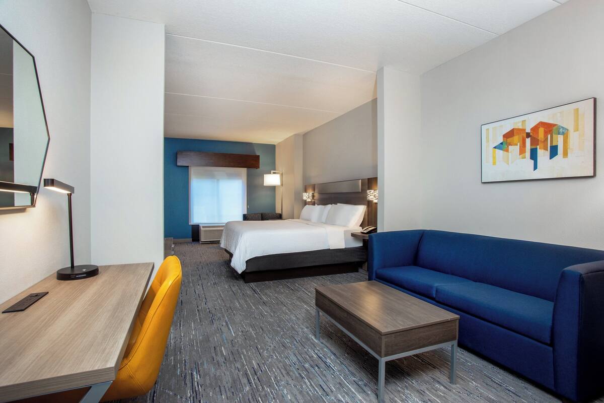 A hotel room with a bed, a blue sofa, a wooden table, a desk, and a chair.