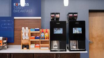 Um espaço para café com duas máquinas de café, uma placa com a inscrição 'EXPRESS START BREAKFAST' e uma seleção de cápsulas e garrafas de café.