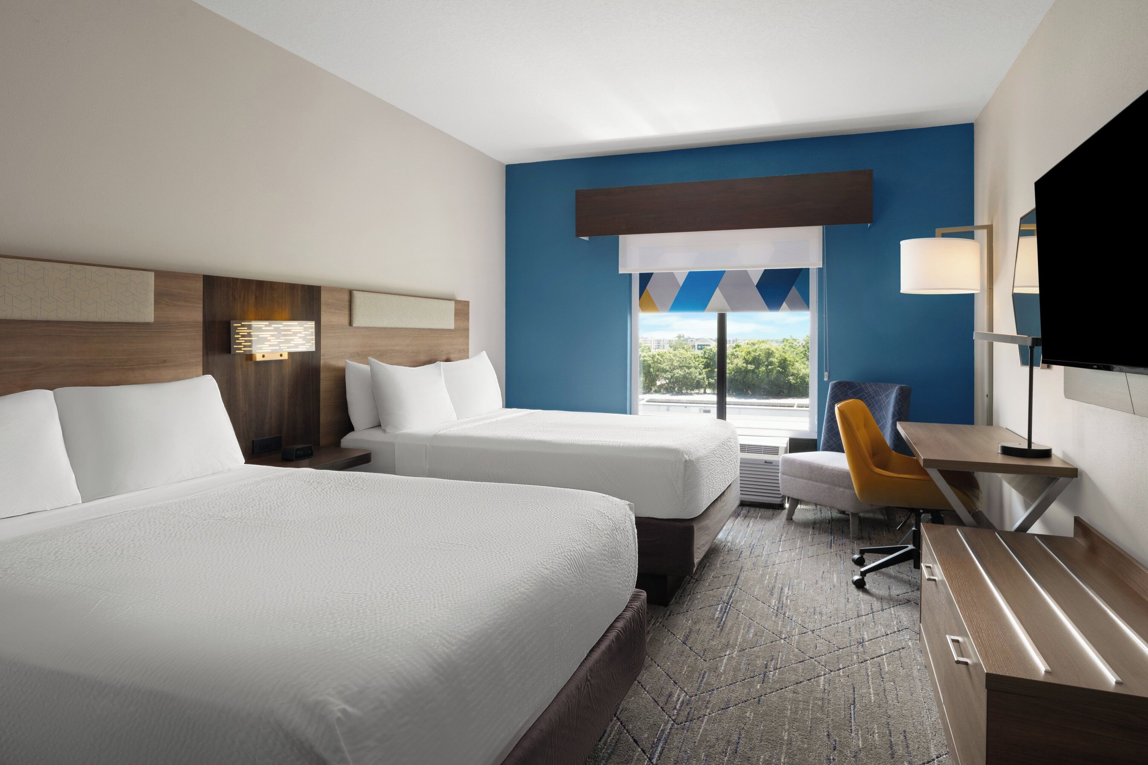 A hotel room with two beds, a desk, a chair, a TV, and a window with a view.