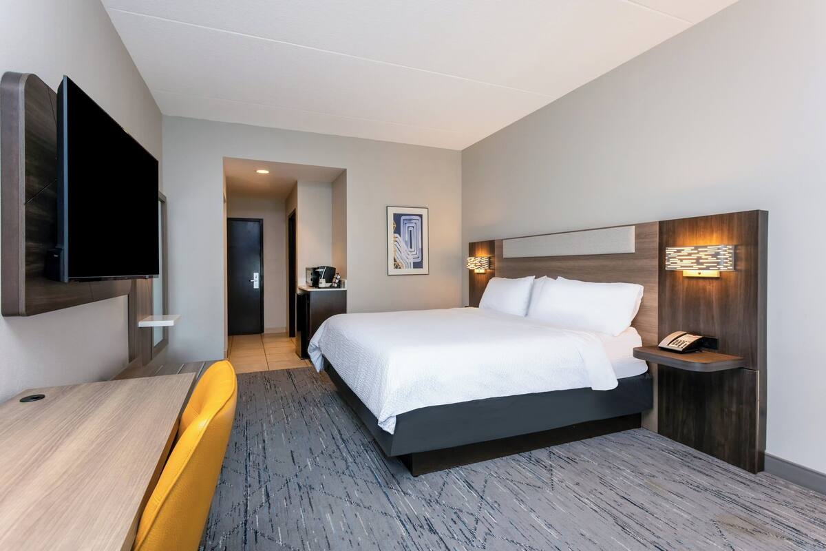 A modern hotel room with a bed, a desk, a chair, a TV, and a wall-mounted phone.
