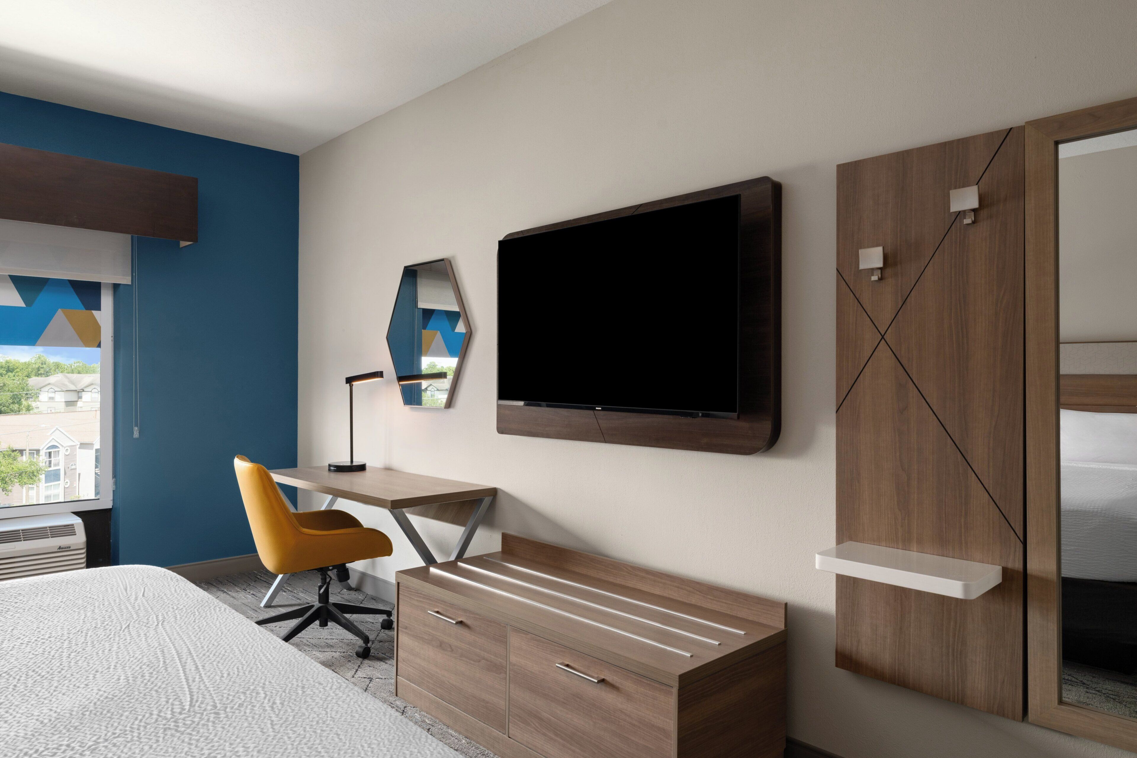 A hotel room with a bed, a desk, a chair, a TV, a wardrobe, and a window with a view.