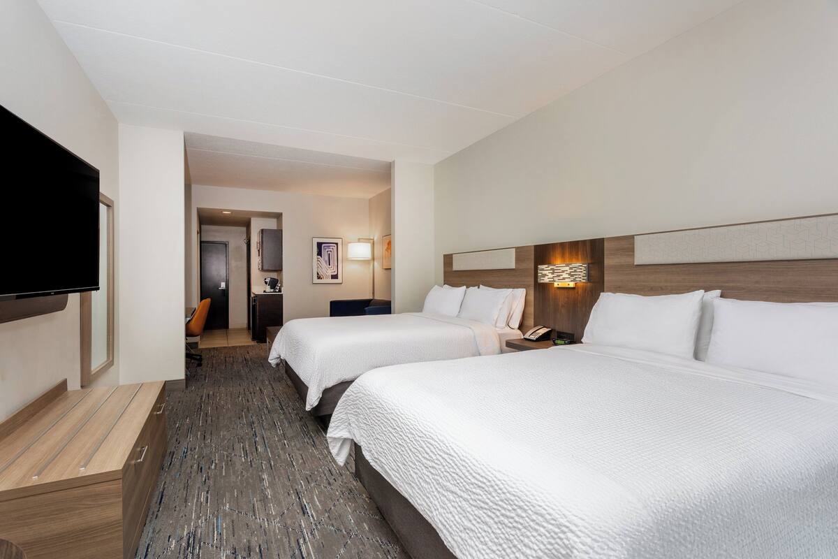 A hotel room with two beds, a flat-screen TV, a desk, and a door leading to a hallway.