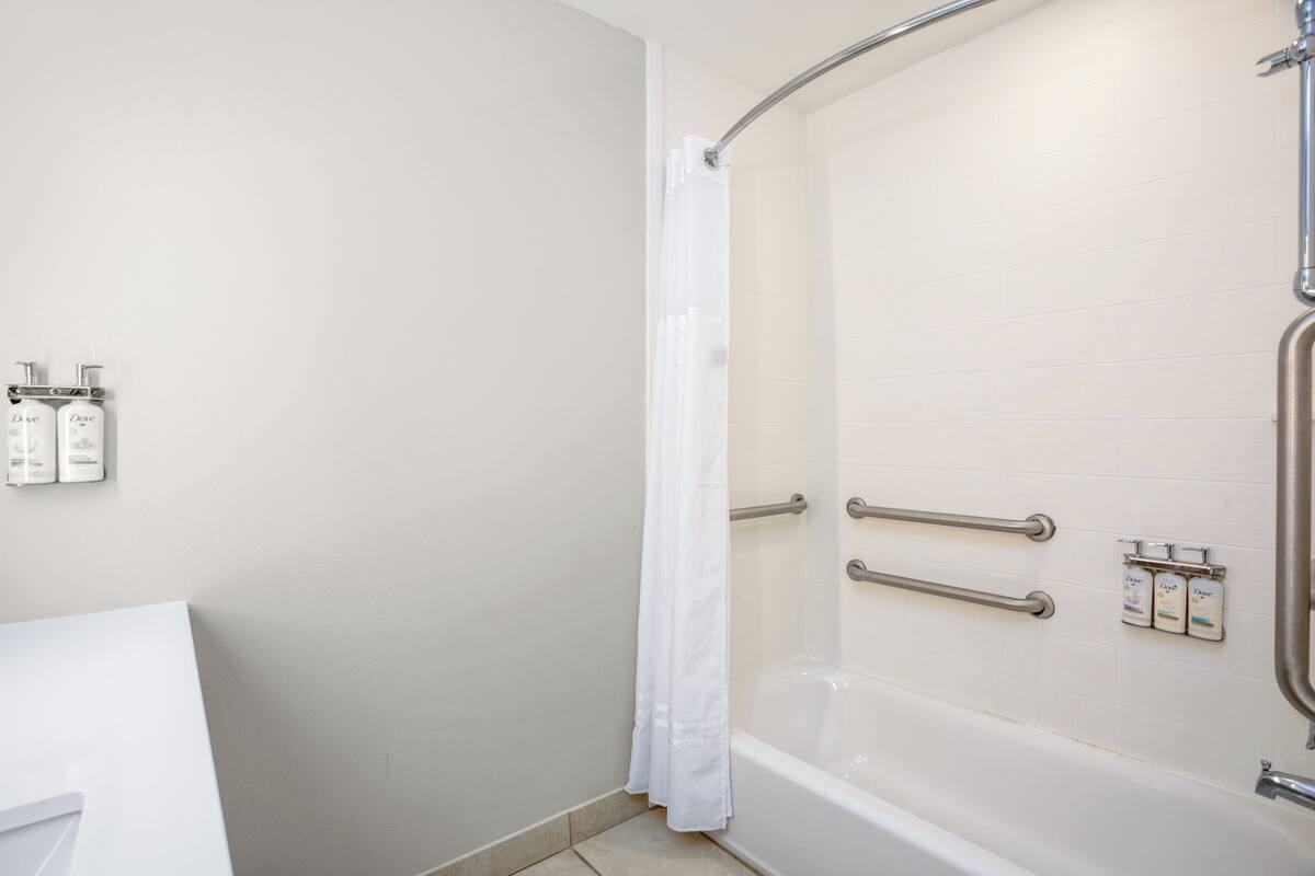 A bathroom with a shower, grab bars, and toiletries on the wall.