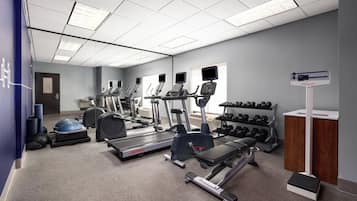 A gym with treadmills, elliptical machines, free weights, and a step platform.