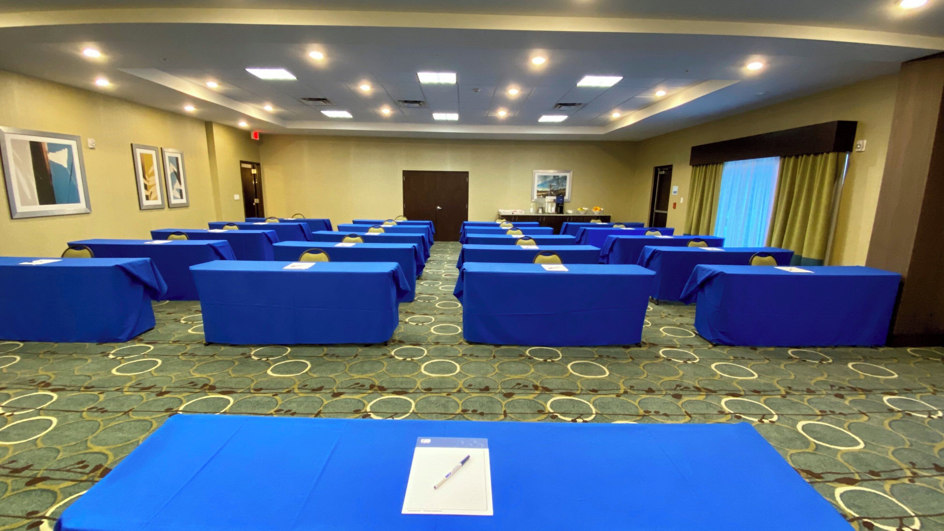 A conference room with rows of tables, a carpeted floor, and a door at the far end.