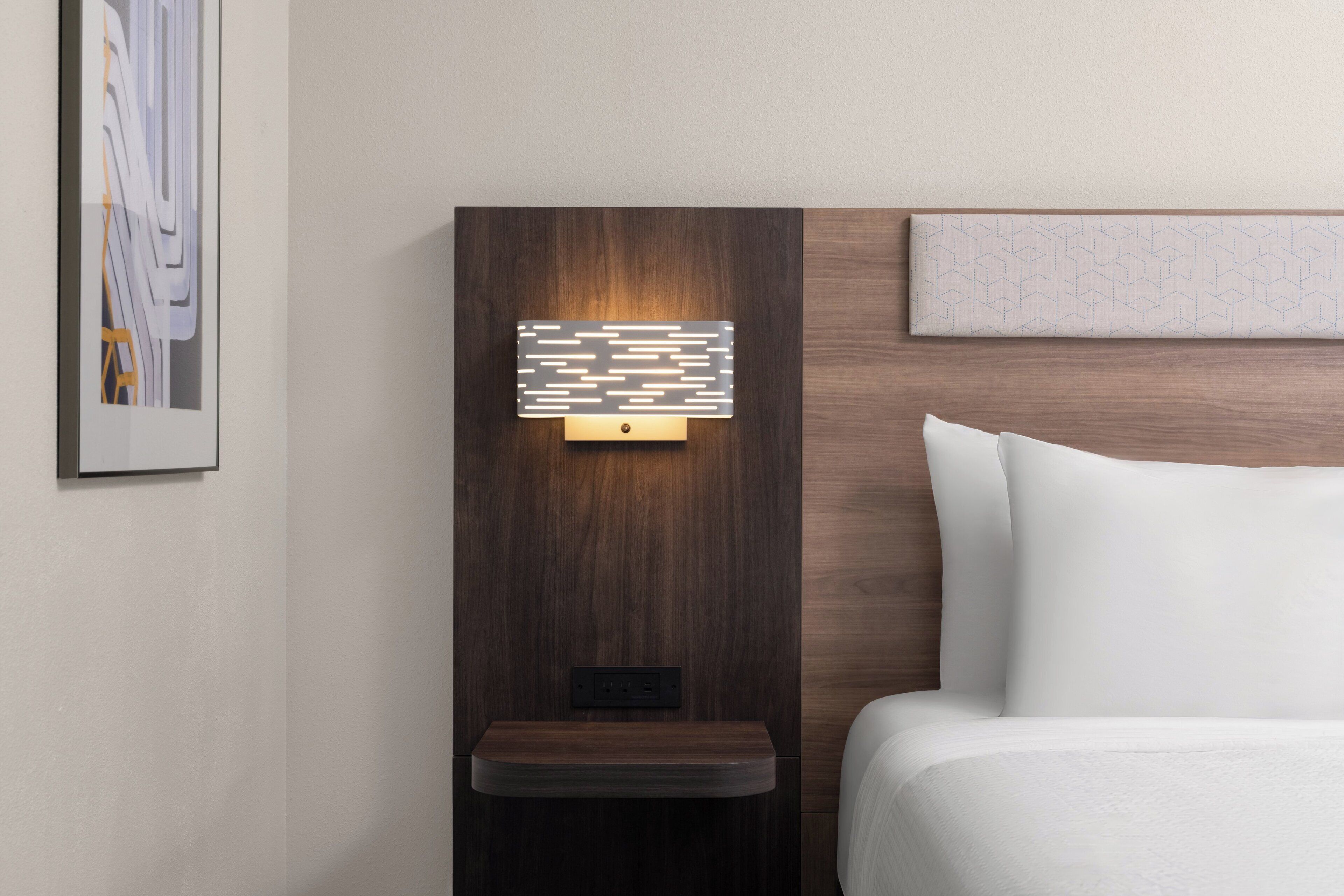 Habitación de hotel moderna con cabecera de madera, una mesita de noche y un aplique de pared.