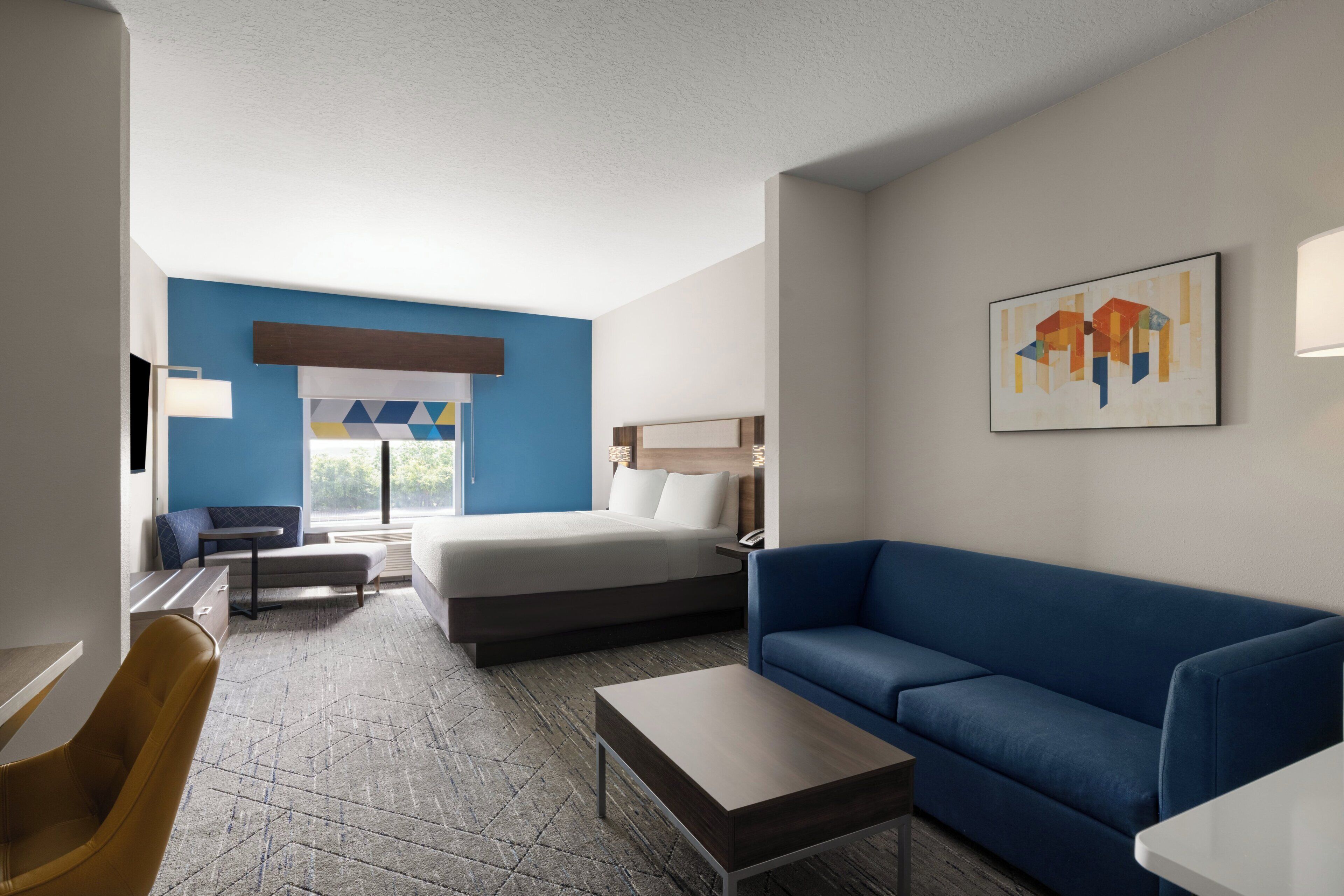 Een hotelkamer met een bed, een blauwe bank, een tafeltje, een stoel en een schilderij aan de muur.