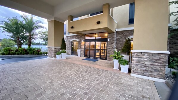 A hotel entrance with a brick-paved driveway, stone and beige exterior walls, and a glass door entrance. - Holiday Inn Express & Suites Orlando East - UCF Area by IHG (Orlando)