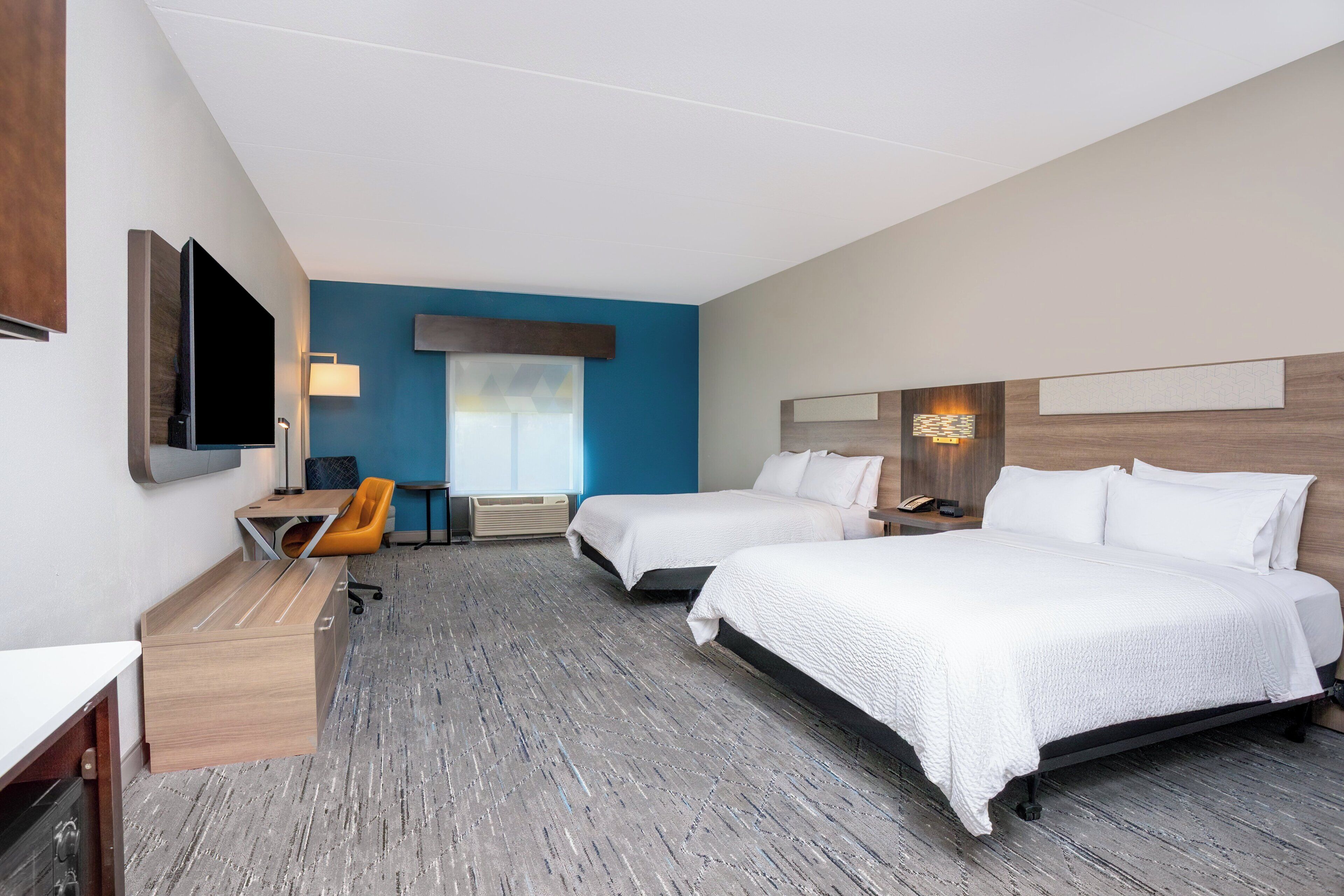 Habitación de hotel con dos camas, un escritorio, una silla, un televisor y una ventana con persianas.
