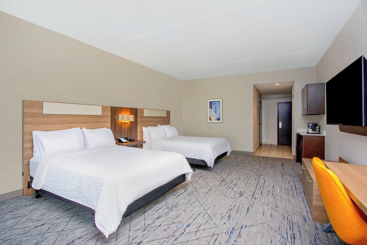 A hotel room with two beds, a desk, a TV, and a door leading to another room.