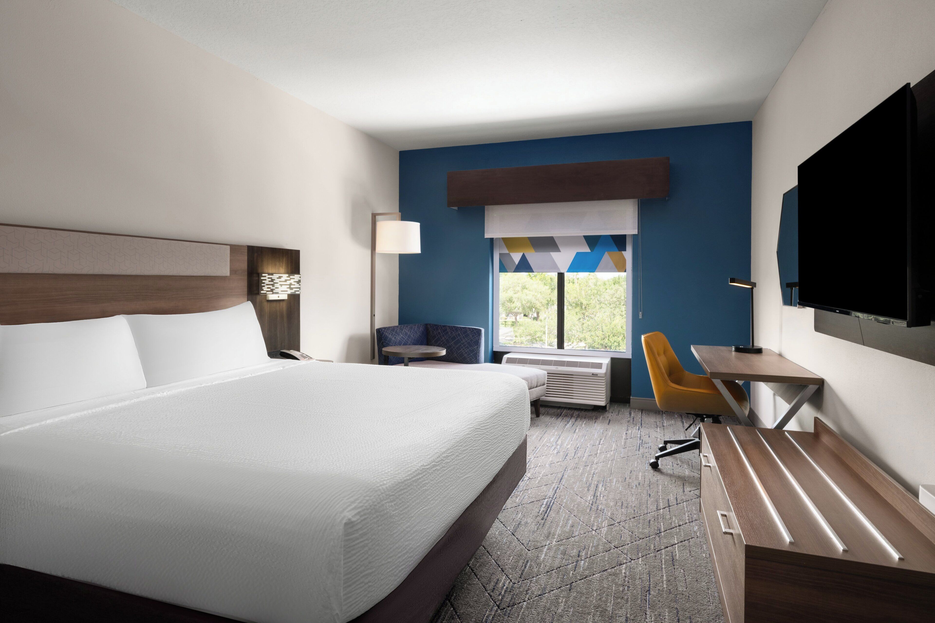 A hotel room with a large bed, a desk, a chair, a TV, and a window with a view.