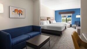 A hotel room with a blue sofa, a bed with white bedding, a small table, and a chair. - Holiday Inn Express & Suites Orlando East - UCF Area by IHG (Orlando)