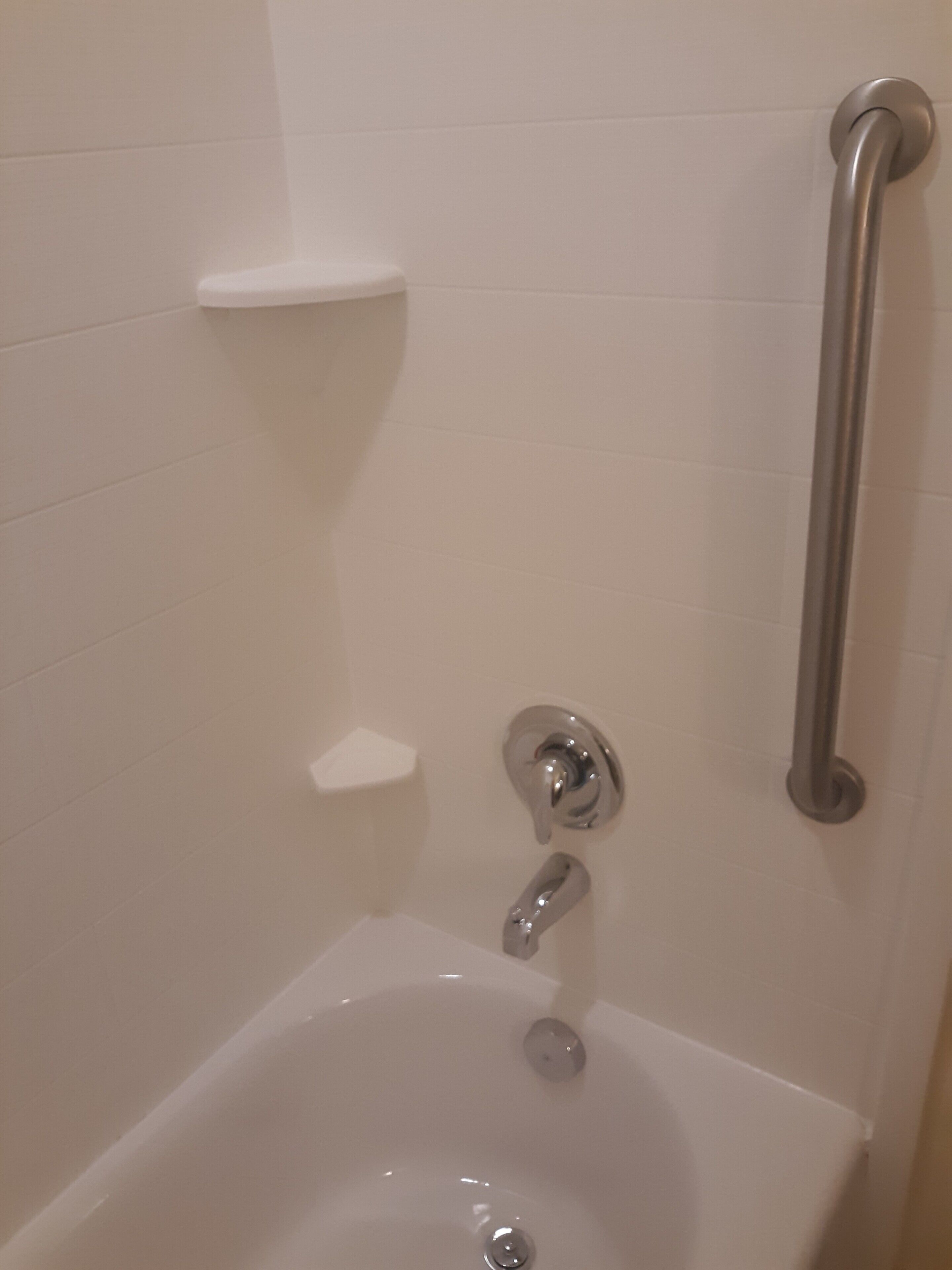 A bathroom with a white bathtub, a grab bar, and a small shelf.