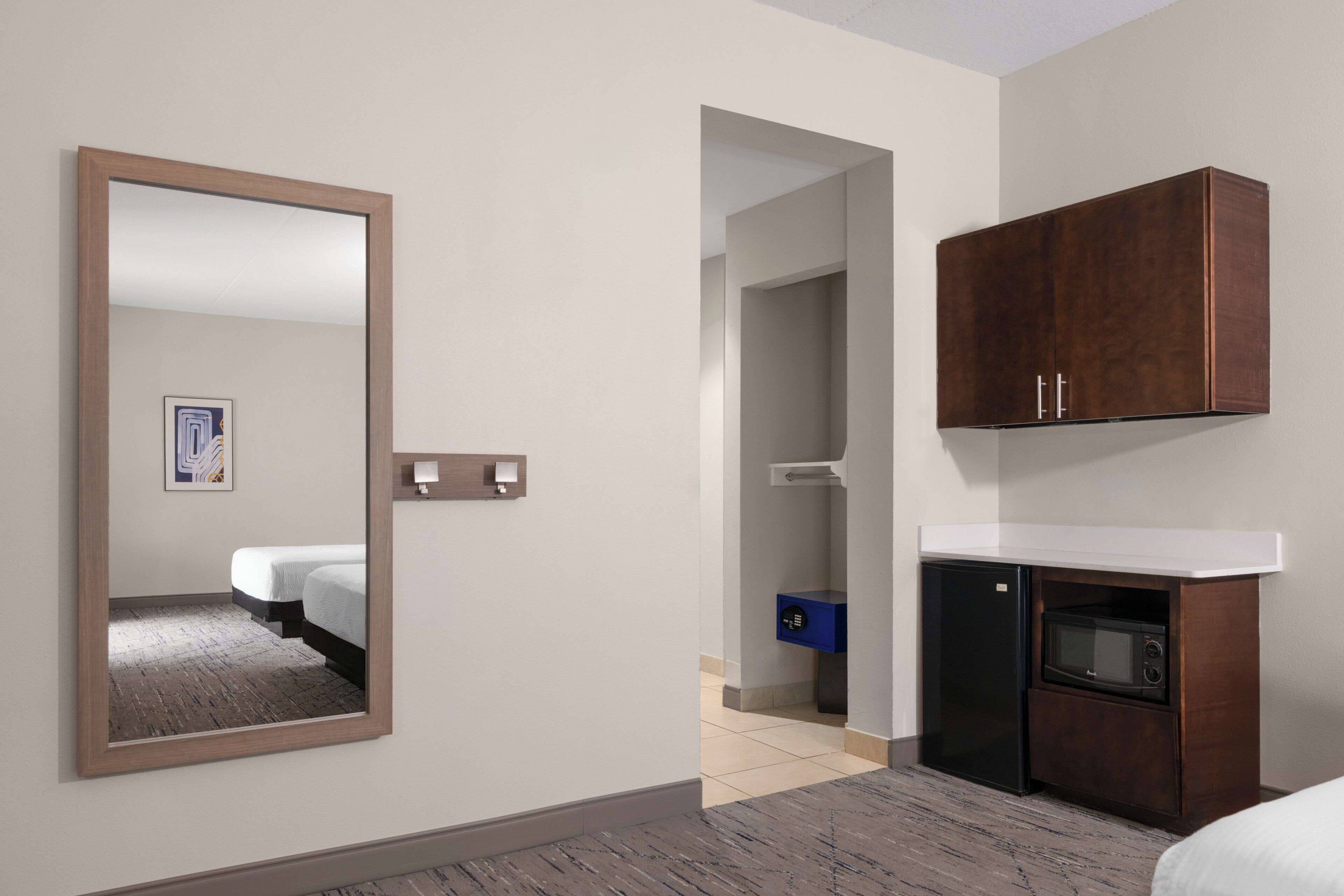 A hotel room with a bed, a mirror, a wardrobe, a microwave, and a small desk area.