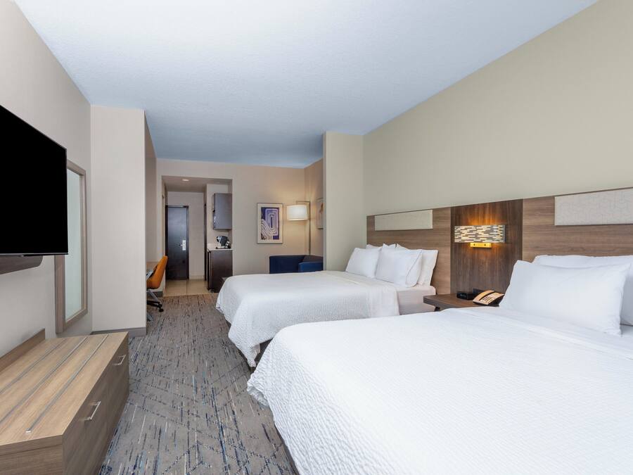 Quarto de hotel com duas camas, televisão de tela plana, escrivaninha e banheiro ao fundo.