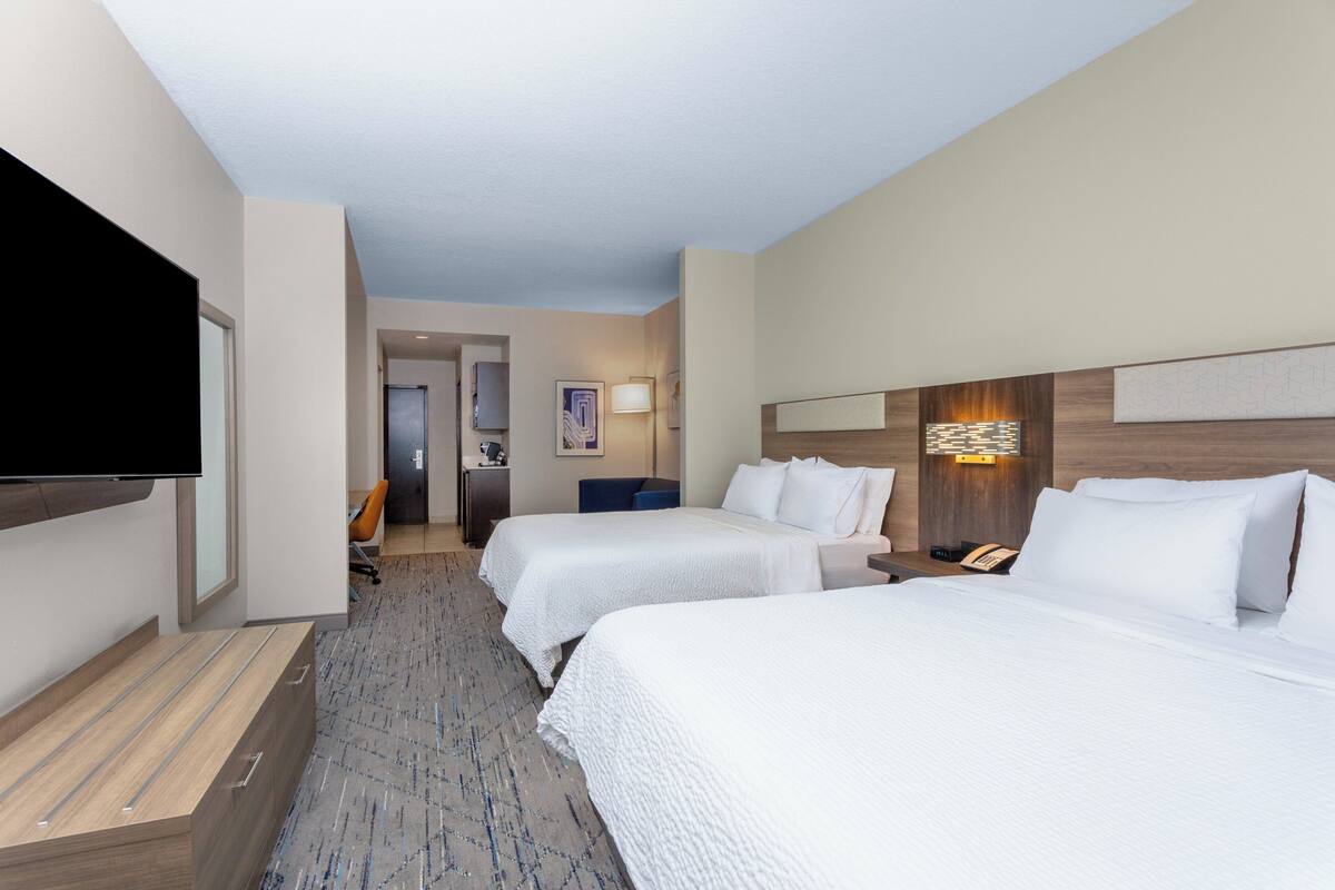 A hotel room with two beds, a flat-screen TV, a desk, and a bathroom visible in the background.