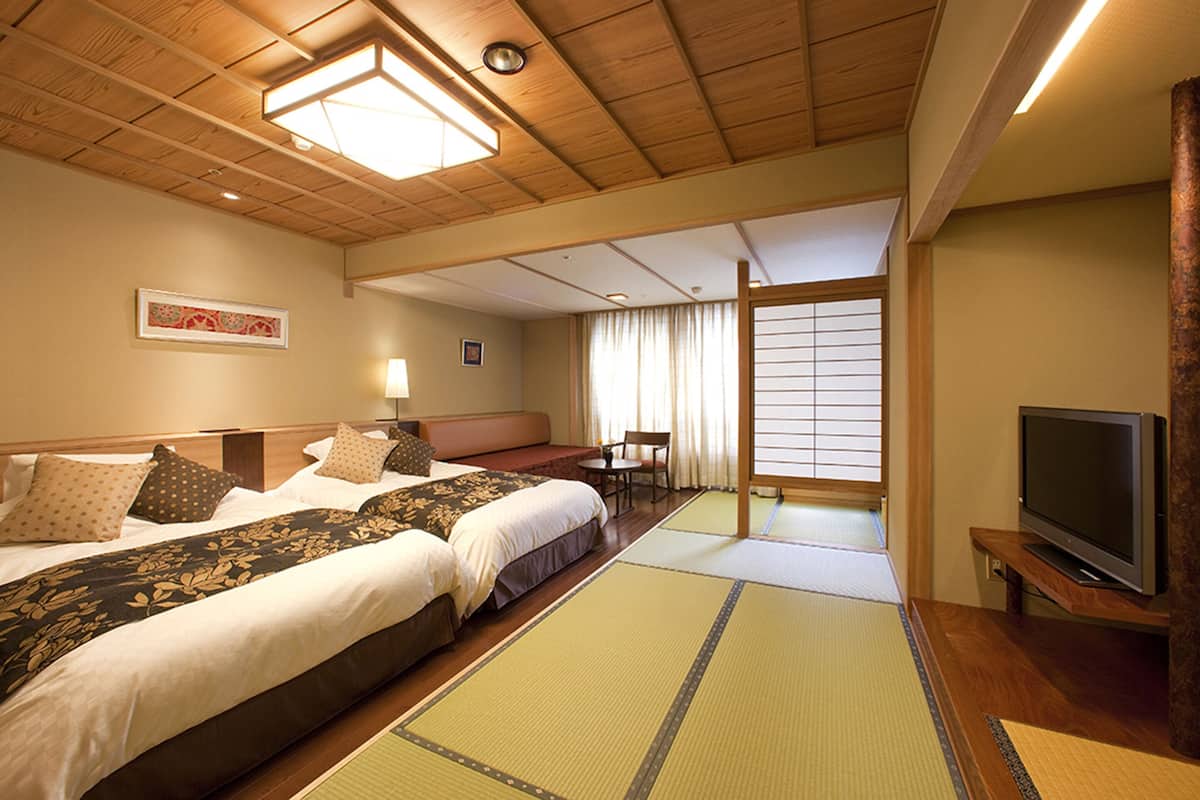 Une chambre d’hôtel avec deux lits, une télévision, des tatamis, une fenêtre avec des rideaux et un plafond en bois.