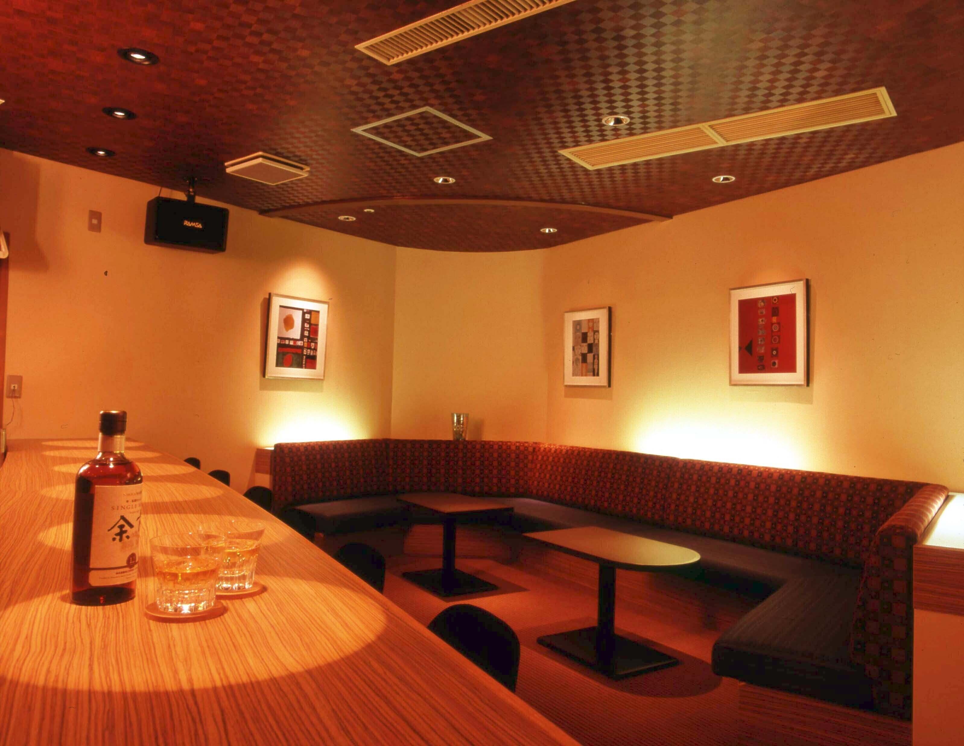 A bar area with wooden flooring, a bar counter, and seating. There are framed pictures on the walls.