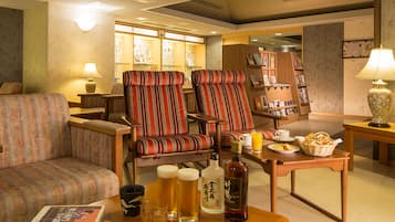 Ein gemütliches Hotelzimmer mit einer Couch, zwei gestreifte Sessel, einem Holztisch mit Getränken und Snacks sowie einem Bücherregal im Hintergrund.