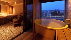Een moderne hotelkamer met een groot bad, een bed en uitzicht op een stadsgezicht door een groot raam.