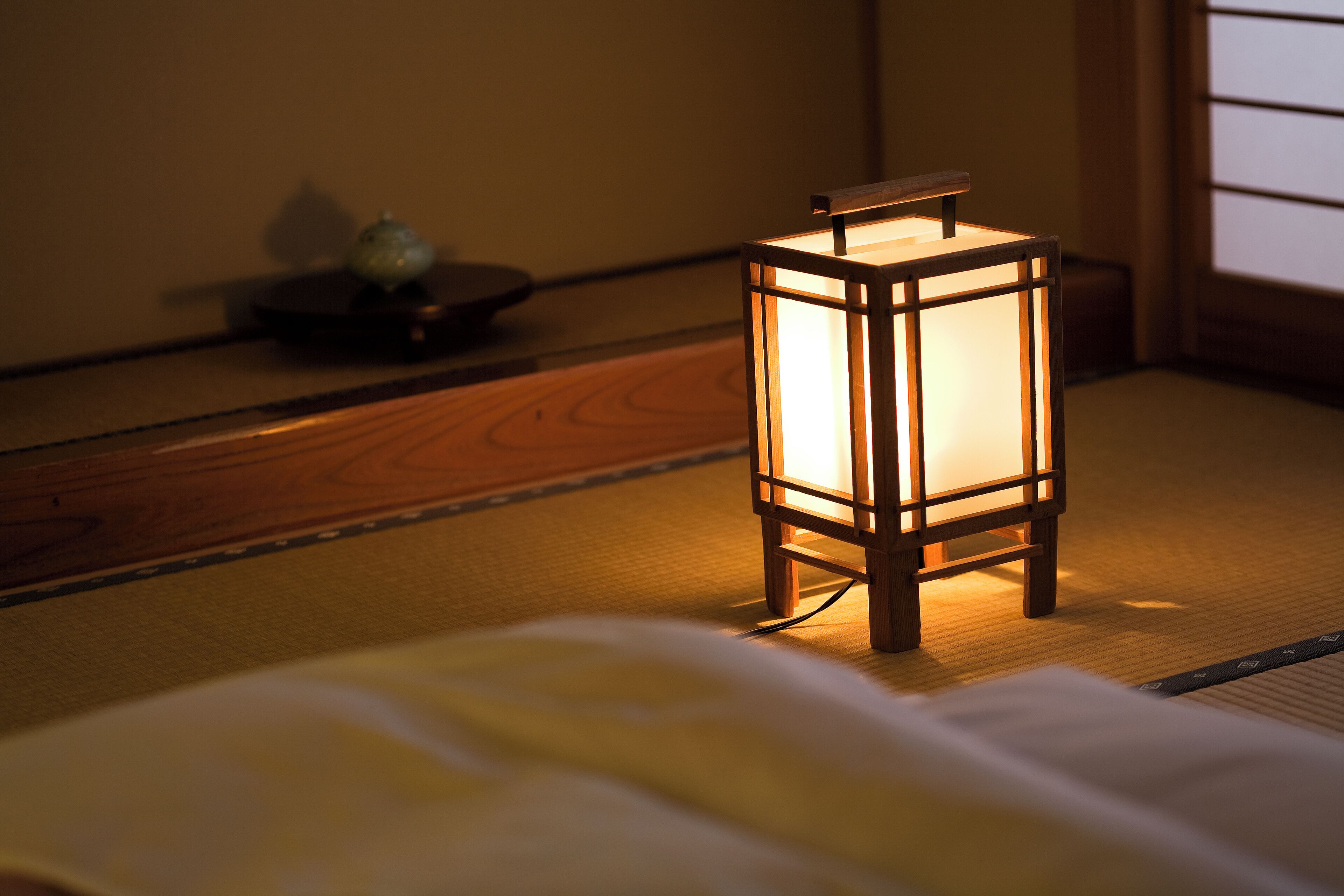 Une pièce de style japonais traditionnel, avec un sol recouvert de tatamis, une lanterne en bois et une petite table agrémentée d’un objet décoratif.