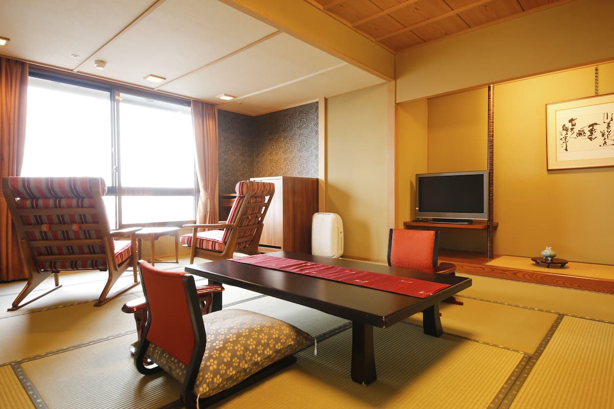 Une pièce de style japonais traditionnel, avec un sol recouvert de tatamis, une table basse et différents types de sièges, notamment un canapé et des fauteuils.