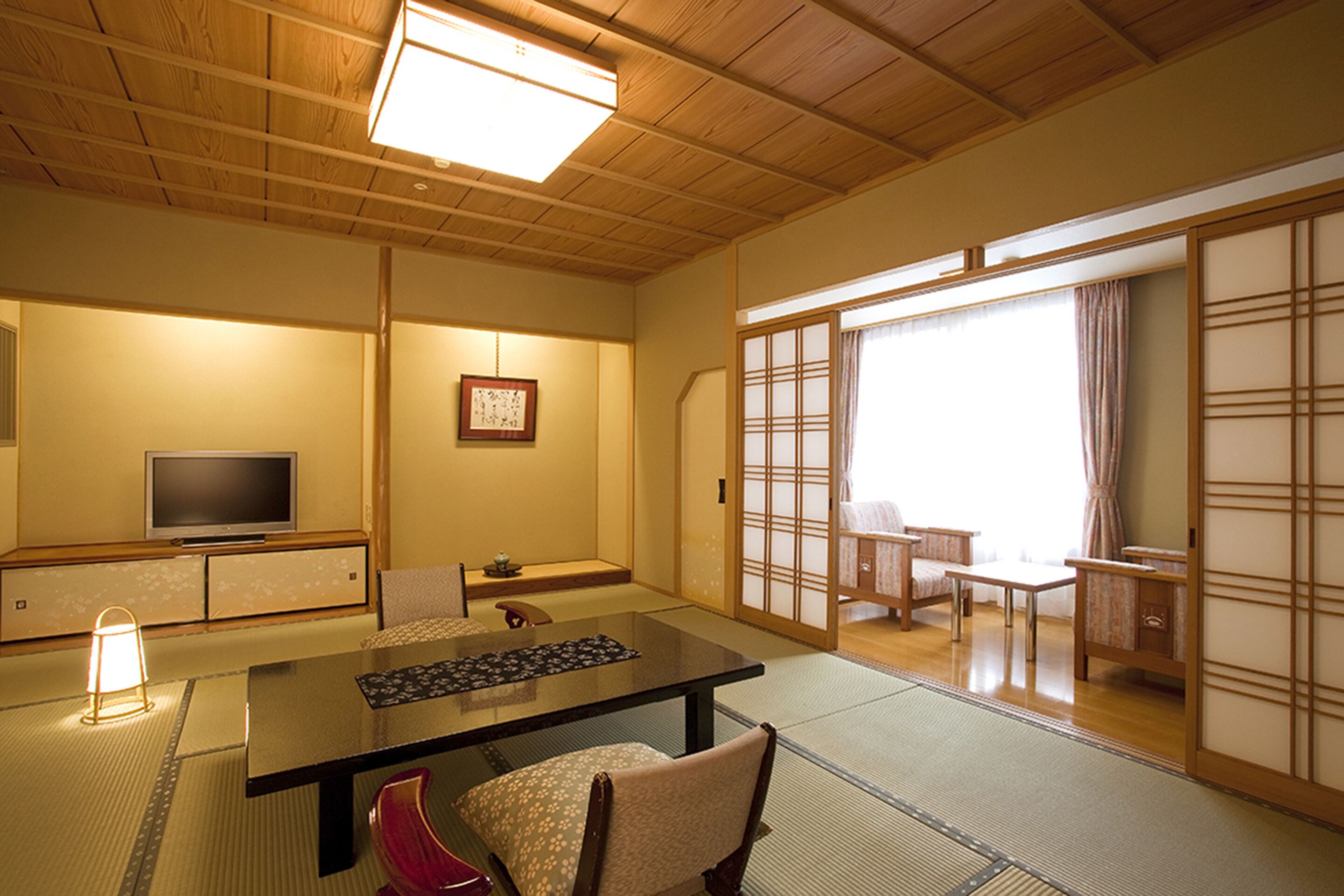 Una habitación japonesa tradicional con suelo de tatami, una mesa baja, un televisor y puertas correderas.