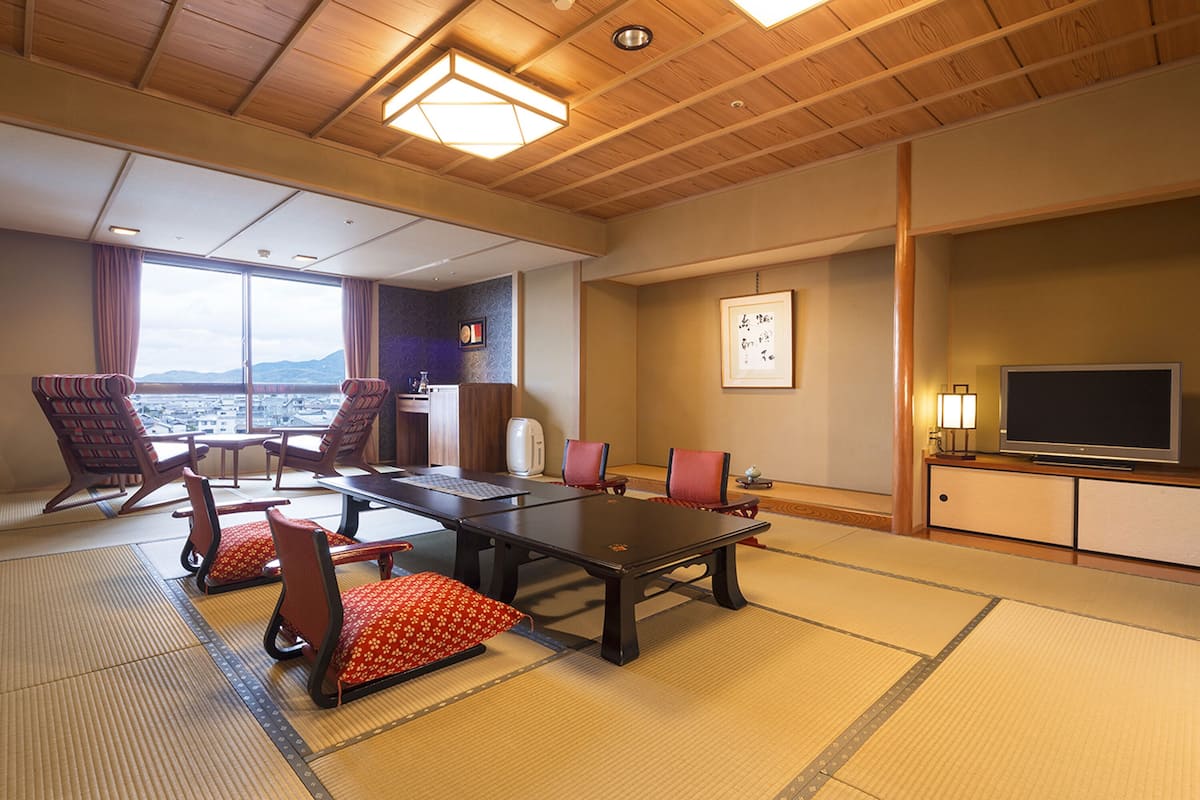 Une pièce de style japonais traditionnel, avec un sol recouvert de tatamis, une table basse et des chaises rembourrées de couleur rouge.